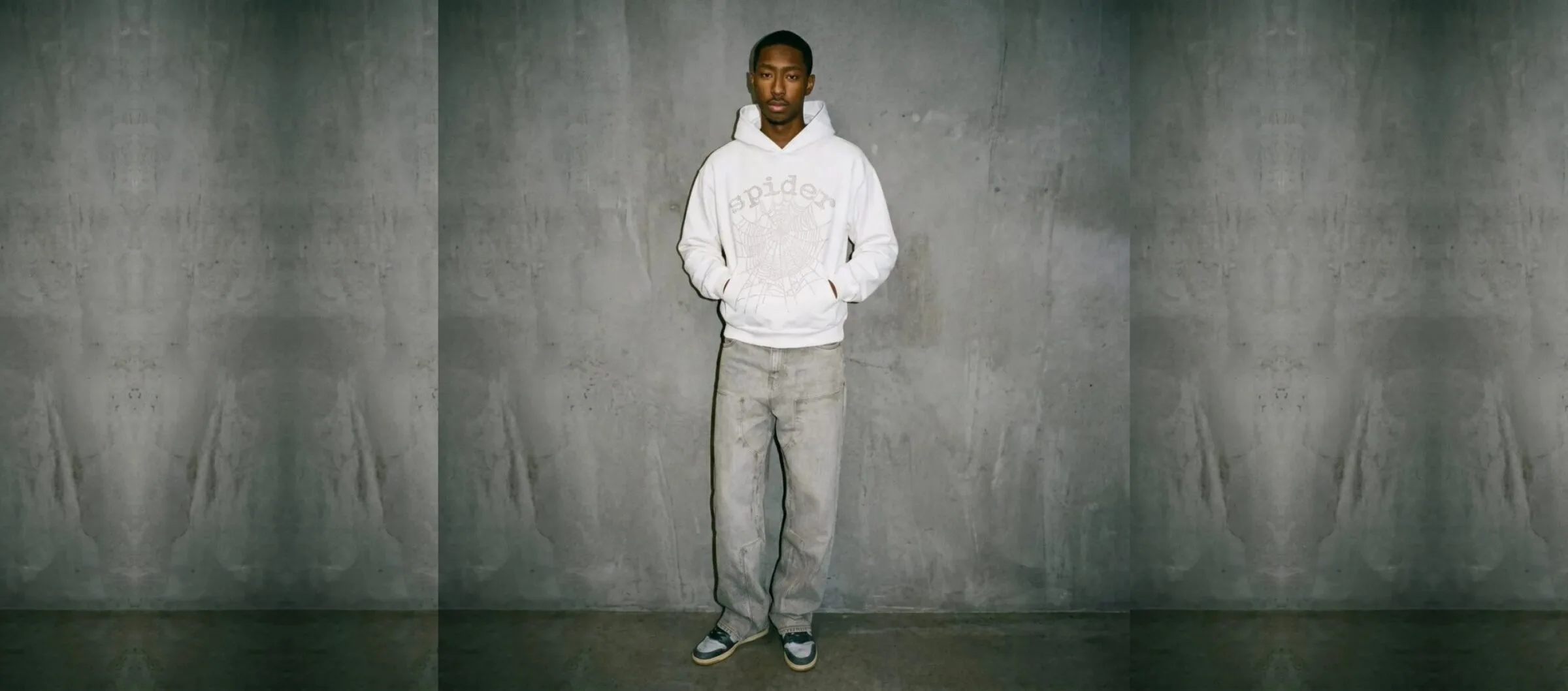 Model in a white Spider rhinestone web hoodie against a concrete wall